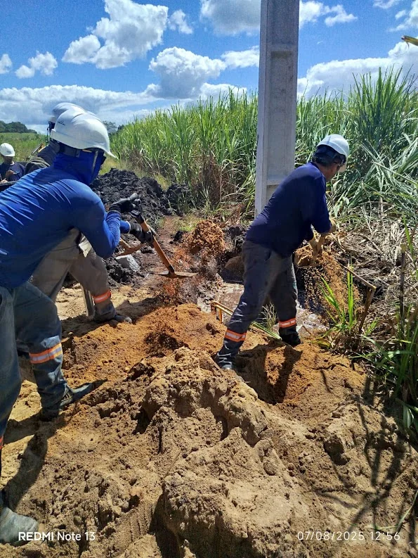 Profissionais de capacete trabalhando junto à base de um poste na Usina Monte Alegre